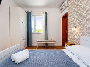 A bedroom with a bed, a bench, a wardrobe, and a window with curtains. - Comfort Two Bedroom Apartment (Pero) (Ploce)