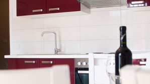 Eine moderne Küche mit weißen und bordeauxfarbenen Schränken, einem Edelstahl-Wasserhahn und einer Weinflasche auf der Arbeitsplatte.
