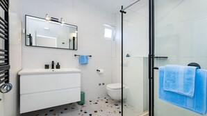 Ein Badezimmer mit einem weißen Waschbecken, einem Spiegel und einer Duschkabine aus Glas.