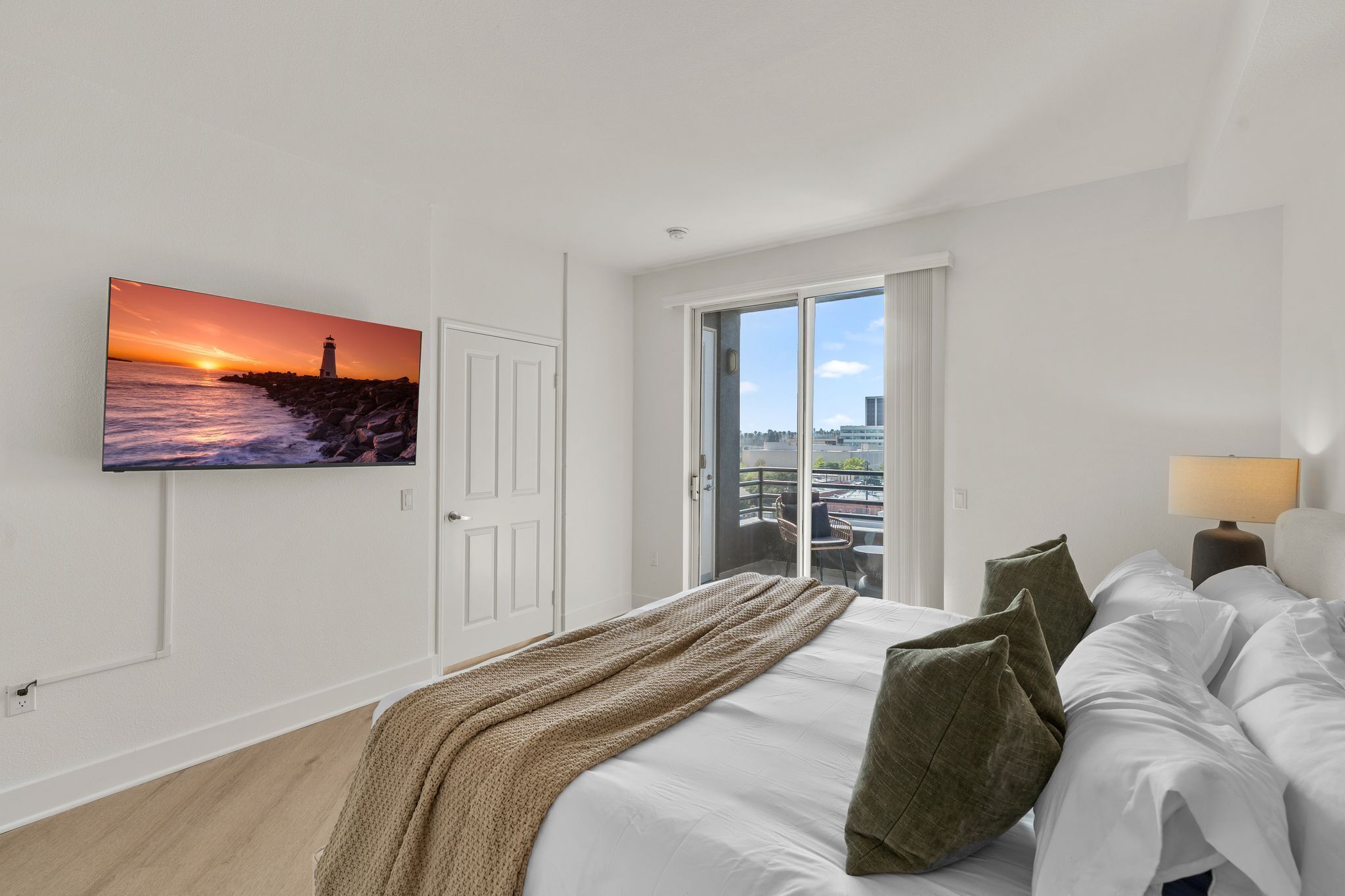 A hotel room with a bed, a television mounted on the wall, a window, and a door.