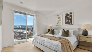 Une chambre avec un grand lit, une table de chevet, une lampe et une vue sur la ville, visible à travers une porte coulissante.