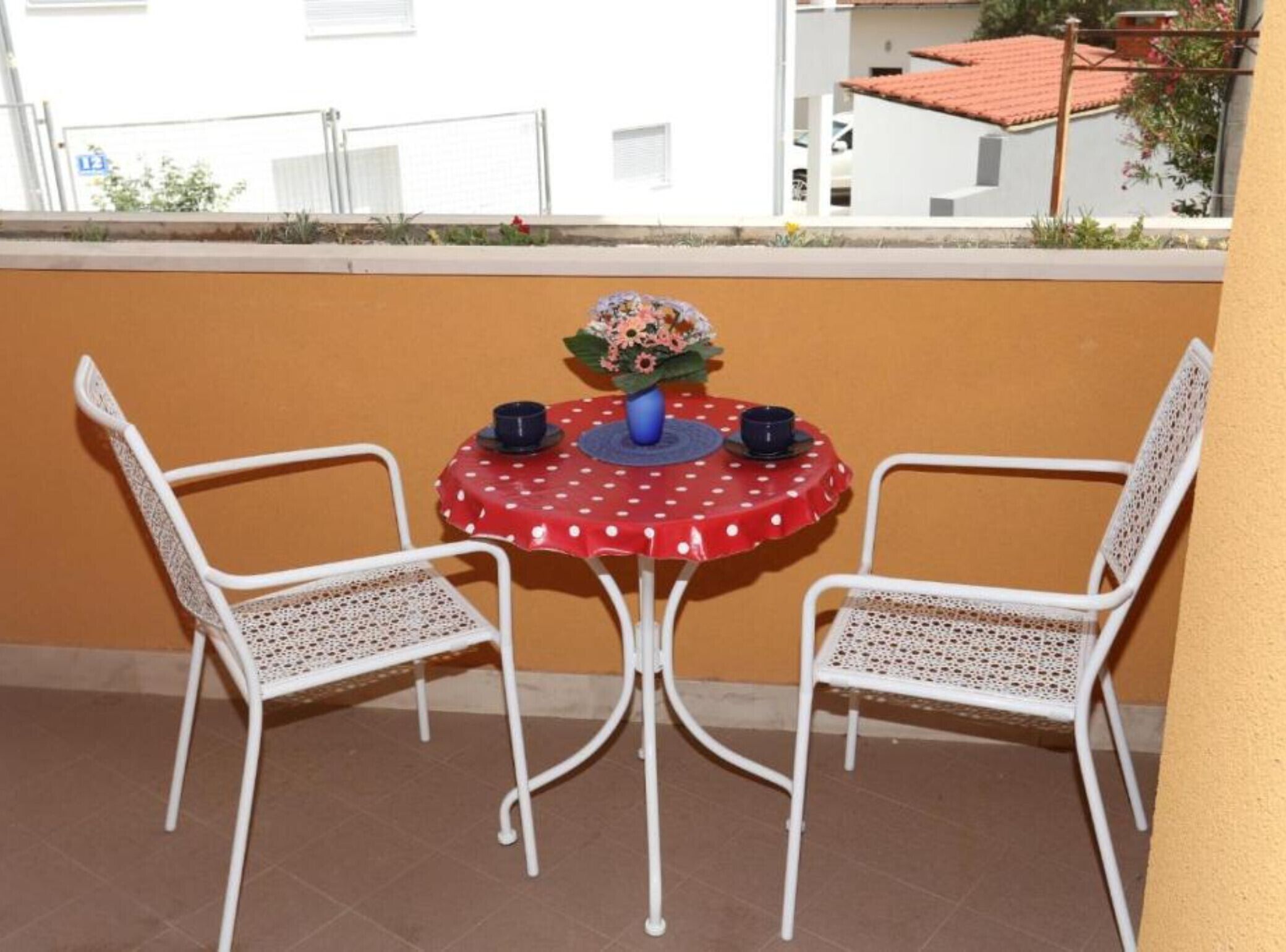 A small round table with a polka dot tablecloth, two white chairs, and a vase with flowers.