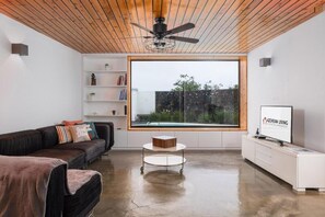 A modern living room with a wooden ceiling, a large window, a sofa, a coffee table, and a TV. - Table Top by Azorean Living (Ponta Delgada, São Miguel)