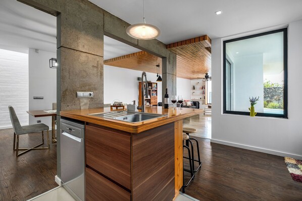 A modern kitchen with a wooden island, built-in dishwasher, and a large window. - Table Top by Azorean Living (Ponta Delgada, São Miguel)