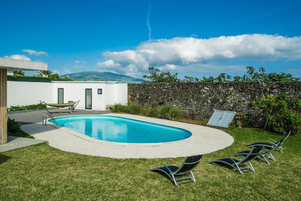 A swimming pool with lounge chairs, a stone wall, and a view of mountains.