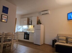 Eine kompakte Küche mit weißen Schränken, einem Backofen und einem Geschirrspüler. Es gibt eine Essecke mit einem Holzbstuhl und einem kleinen Tisch.