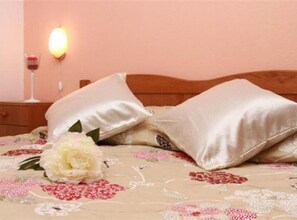 Ein Bett mit weißen Kissen, einer blumigen Tagesdecke und einem Nachttisch mit einem Weinglas.