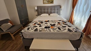 A bedroom with a bed, a bedside table, a wardrobe, a painting on the wall, and a window with curtains. - One bedroom apartment (702) (Orebic)