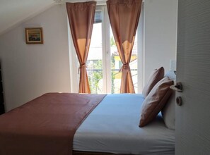 Ein Schlafzimmer mit Bett, Vorhängen, einer Tür und einem Fenster.