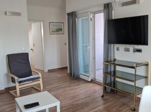 Ein Zimmer mit einem Sessel, einem kleinen Tisch, einem Fernseher und einer Schiebetür.