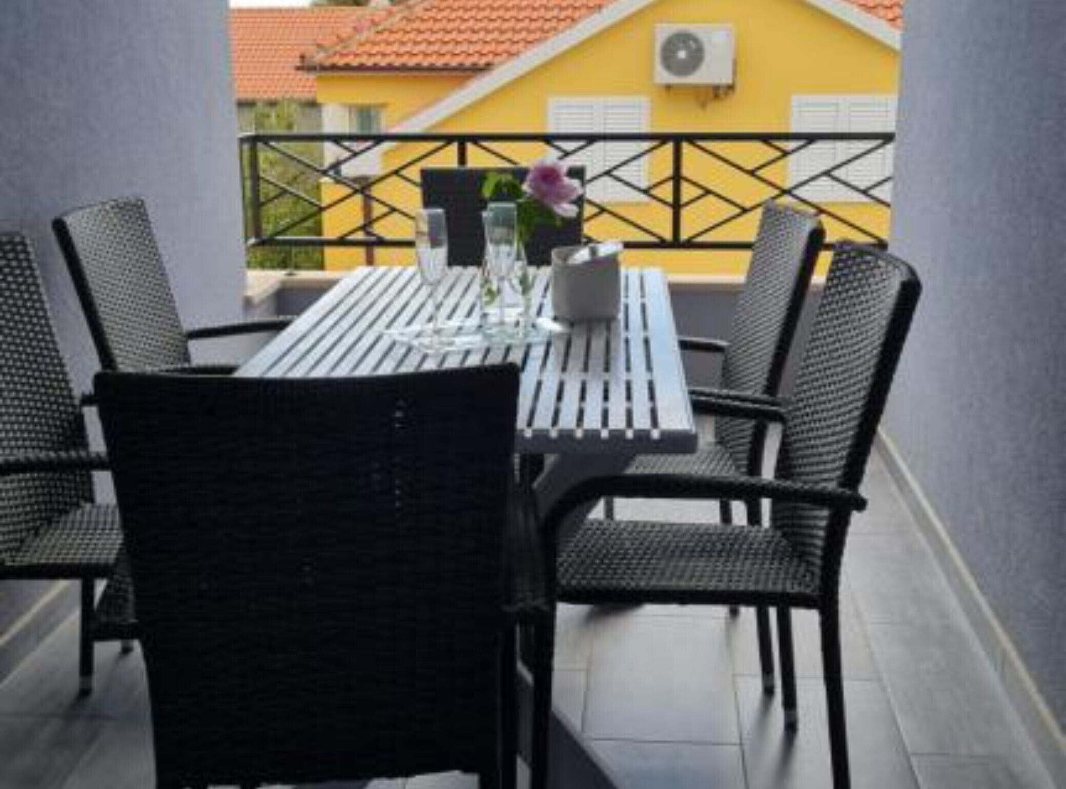 Ein Balkon mit Tisch und Stühlen, im Hintergrund ein gelbes Gebäude und ein schwarzes Geländer.