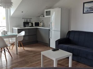 Ein kompakter Wohnbereich mit Küchenzeile, einem Essbereich mit Glastisch, einem dunkelgrauen Sofa und einem weißen Couchtisch.