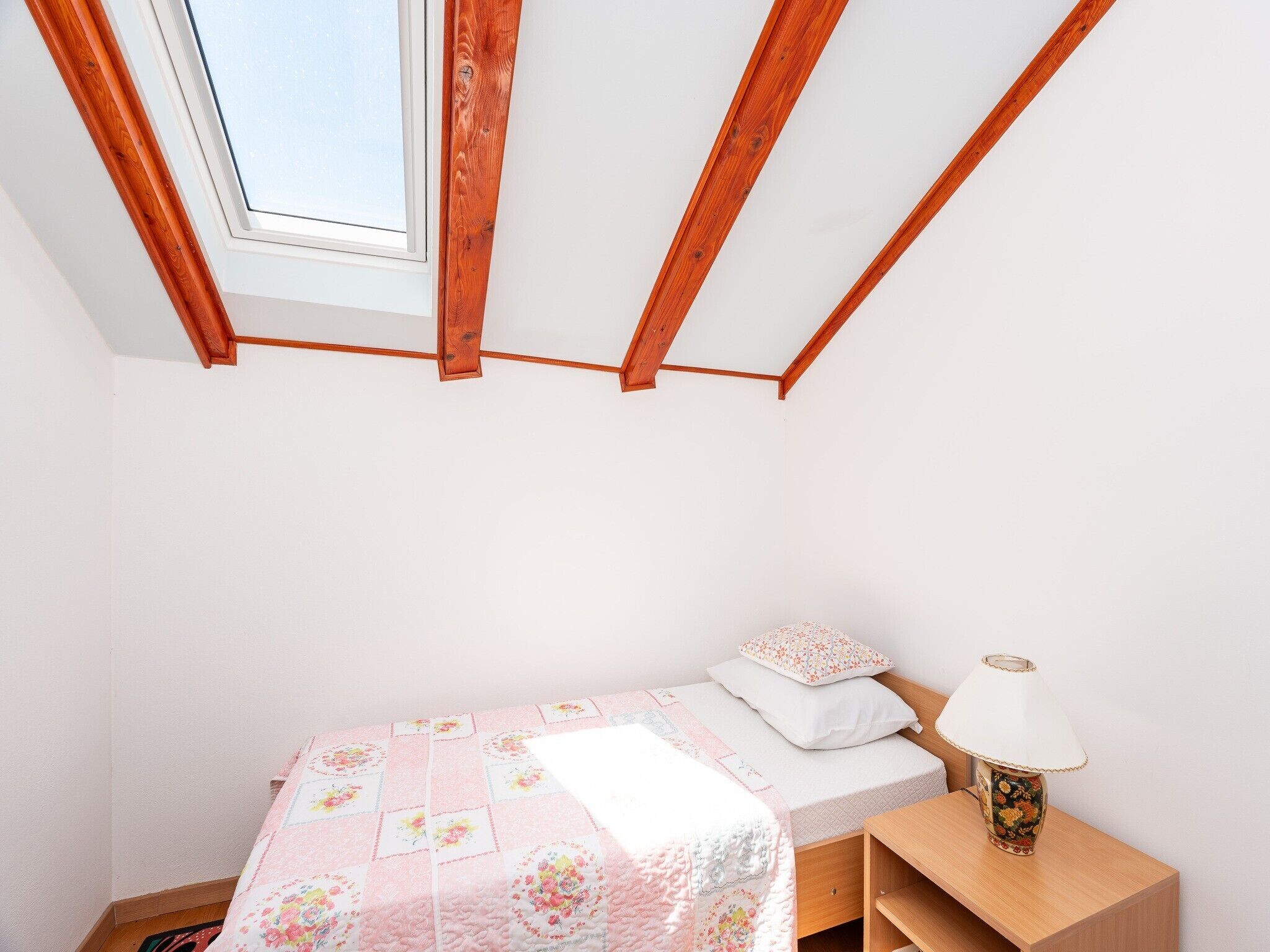 Ein Schlafzimmer mit Dachfenster, einem Bett mit floralem Bettzeug, einer Nachttischlampe und einem Holznachttisch.