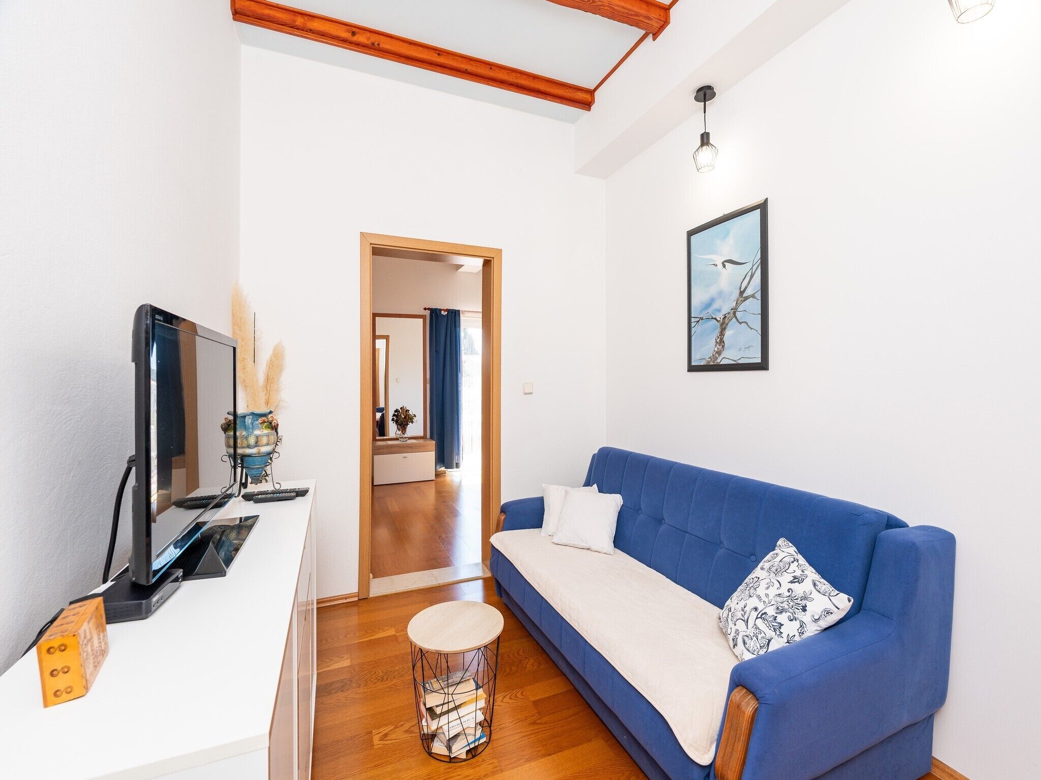 A modern living room with a blue sofa, a flat-screen TV, and a small round table with books.