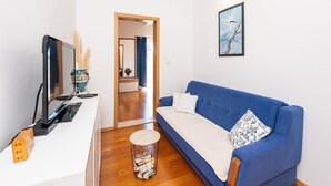 Een moderne woonkamer met een blauwe bank, een flatscreen televisie en een klein, rond tafeltje met boeken.