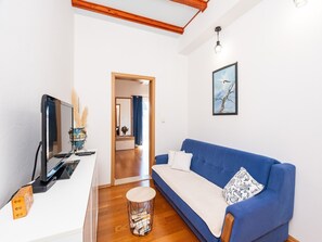 Ein modernes Wohnzimmer mit einem blauen Sofa, einem Flachbildfernseher und einem kleinen runden Tisch mit Büchern.