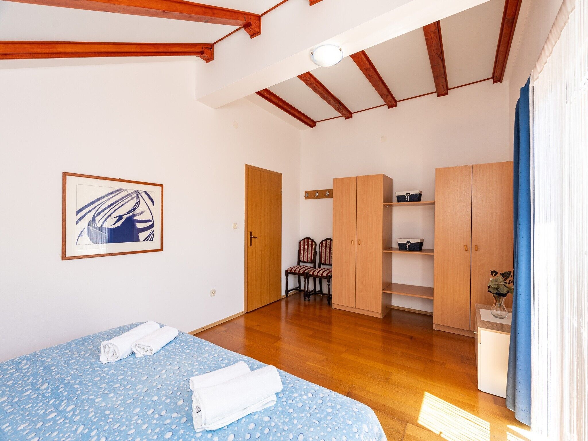 A bedroom with a bed, a wardrobe, a chair, and a framed picture on the wall.