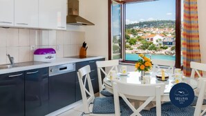 Eine moderne Küche mit Blick auf eine Küstenstadt, ein Essbereich mit Tisch für zwei Personen und ein großes Fenster mit Vorhängen.