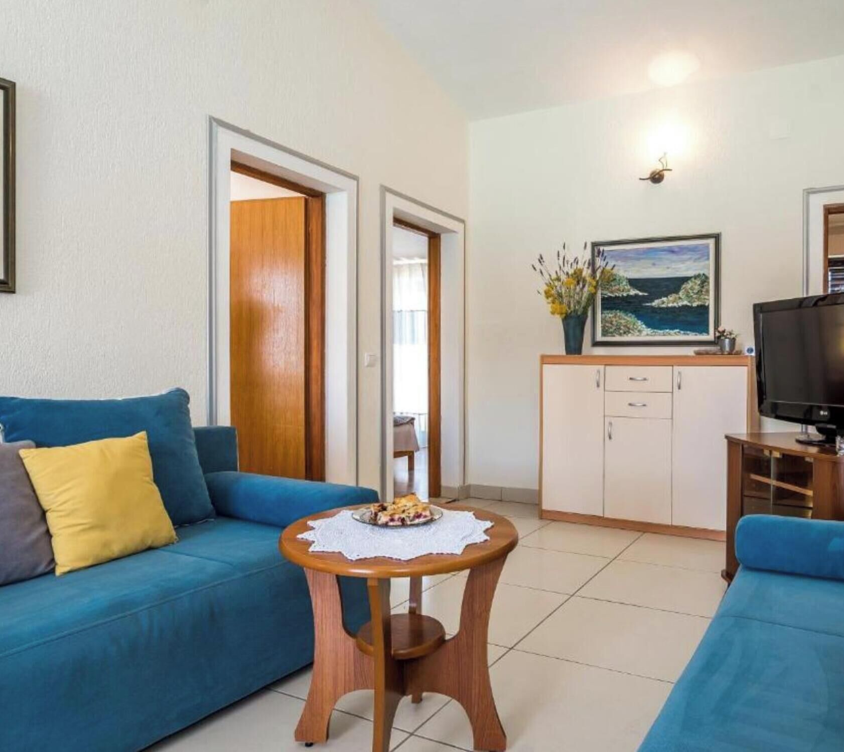 Una sala de estar con un sofá, una mesa de centro con un plato de comida, un televisor, un armario y un cuadro en la pared.