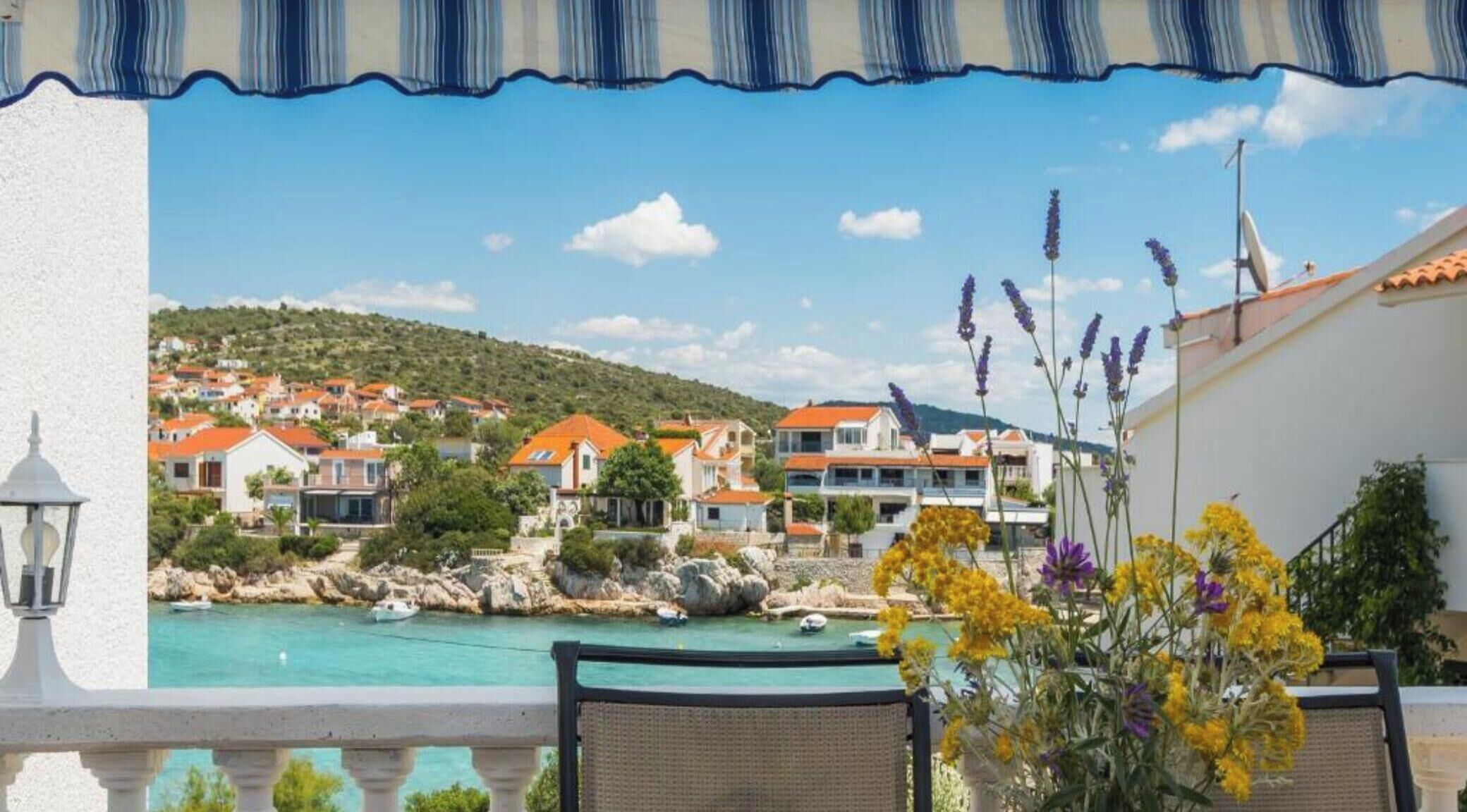 A coastal view with a balcony, a pool, and a hillside of houses.