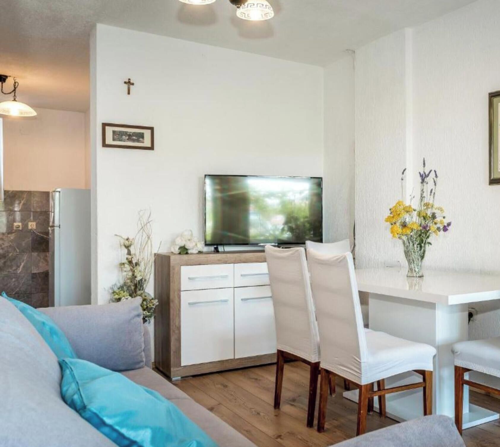 A modern living room with a sofa, a dining table, a TV, and a cross on the wall.