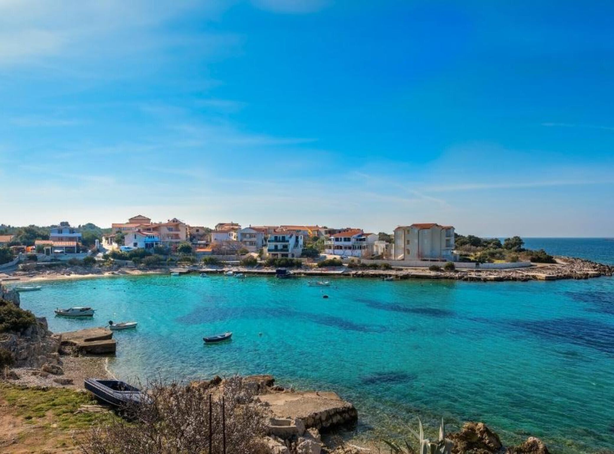 Una cittadina costiera con edifici lungo la costa, barche sull'acqua e cielo sereno.
