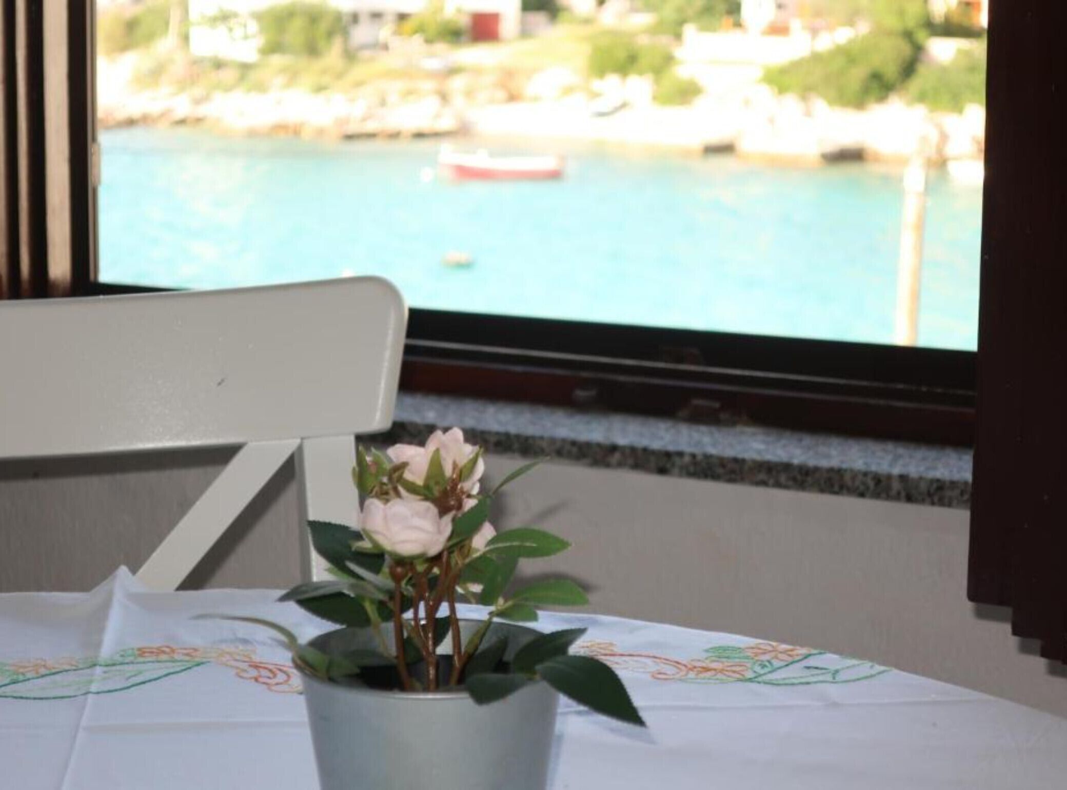 Una planta en test amb un taulell, una finestra amb vista a un cos d'aigua i barques, i una cadira blanca.