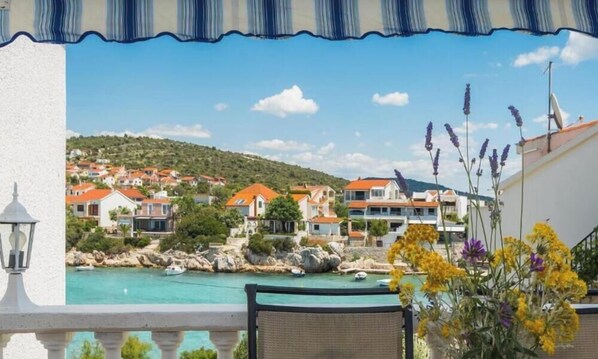 A balcony with a view of a coastal town, a pool, and a flower arrangement.