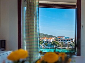 Ein Zimmer mit Blick auf eine Küstenstadt, ein Fenster mit Vorhängen und eine Vase mit gelben Blumen.