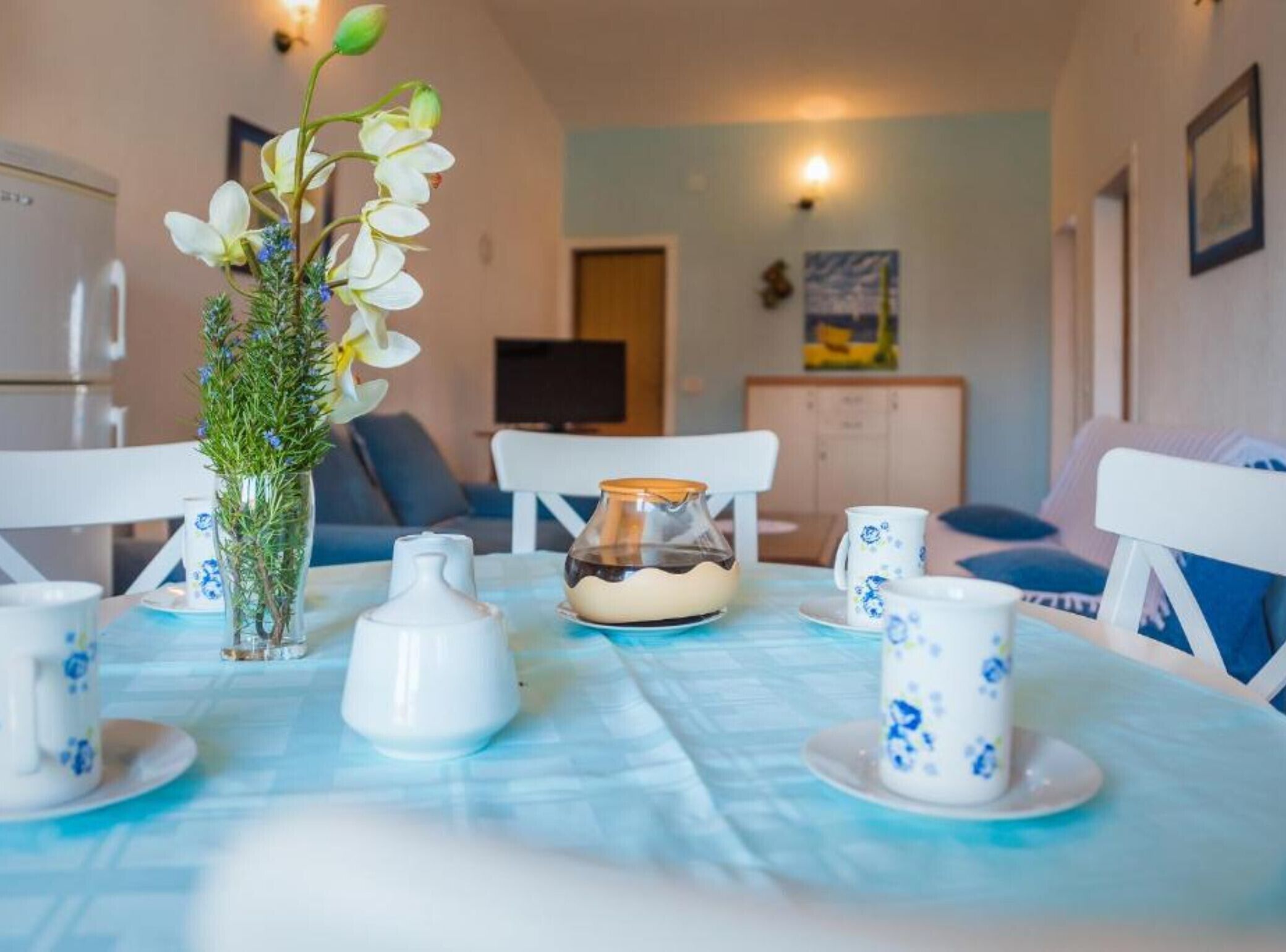 A dining table with white and blue floral tableware, a glass pitcher, and a vase with white flowers.