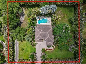 Vista aérea de una propiedad con piscina, un edificio hexagonal y abundante vegetación.