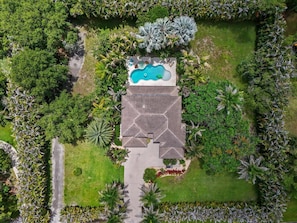 An aerial view of a property with a swimming pool, surrounded by lush greenery and a geometric roof structure.