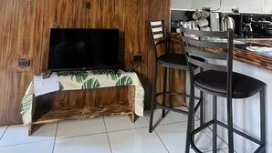 A modern kitchen with a wooden accent wall, a dining area with chairs, and a flat-screen TV. - Cozy 1-bedroom cabin in quaint San Carlos with AC (San Carlos)