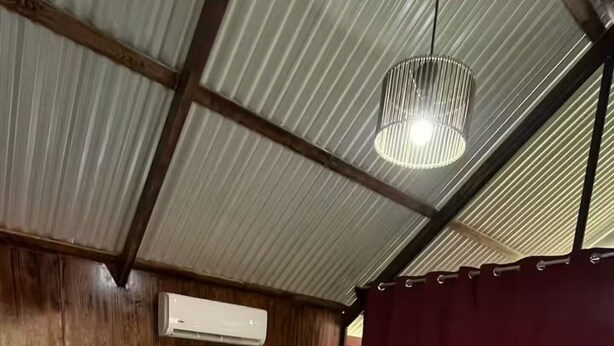 A hotel room with a bed, a nightstand, a red curtain, and a hanging light fixture. - Cozy 1-bedroom cabin in quaint San Carlos with AC (San Carlos)