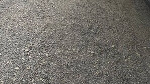 Um espaço ao ar livre coberto com piso de cascalho, cerca de madeira e estrutura de telhado metálico.