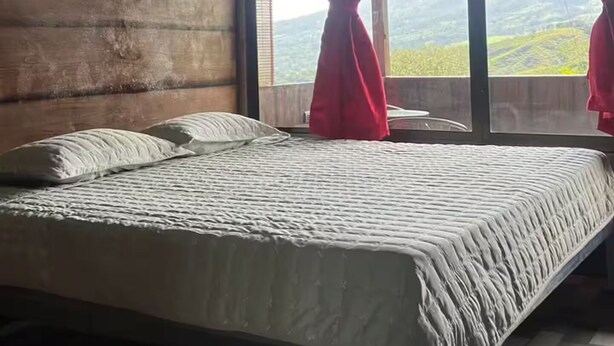 Quarto com cama, ventilador de teto e vista para o exterior.