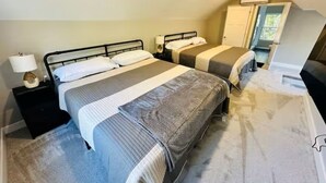 Een slaapkamer met twee bedden, een nachtkastje, een lamp en een deur naar een andere kamer.