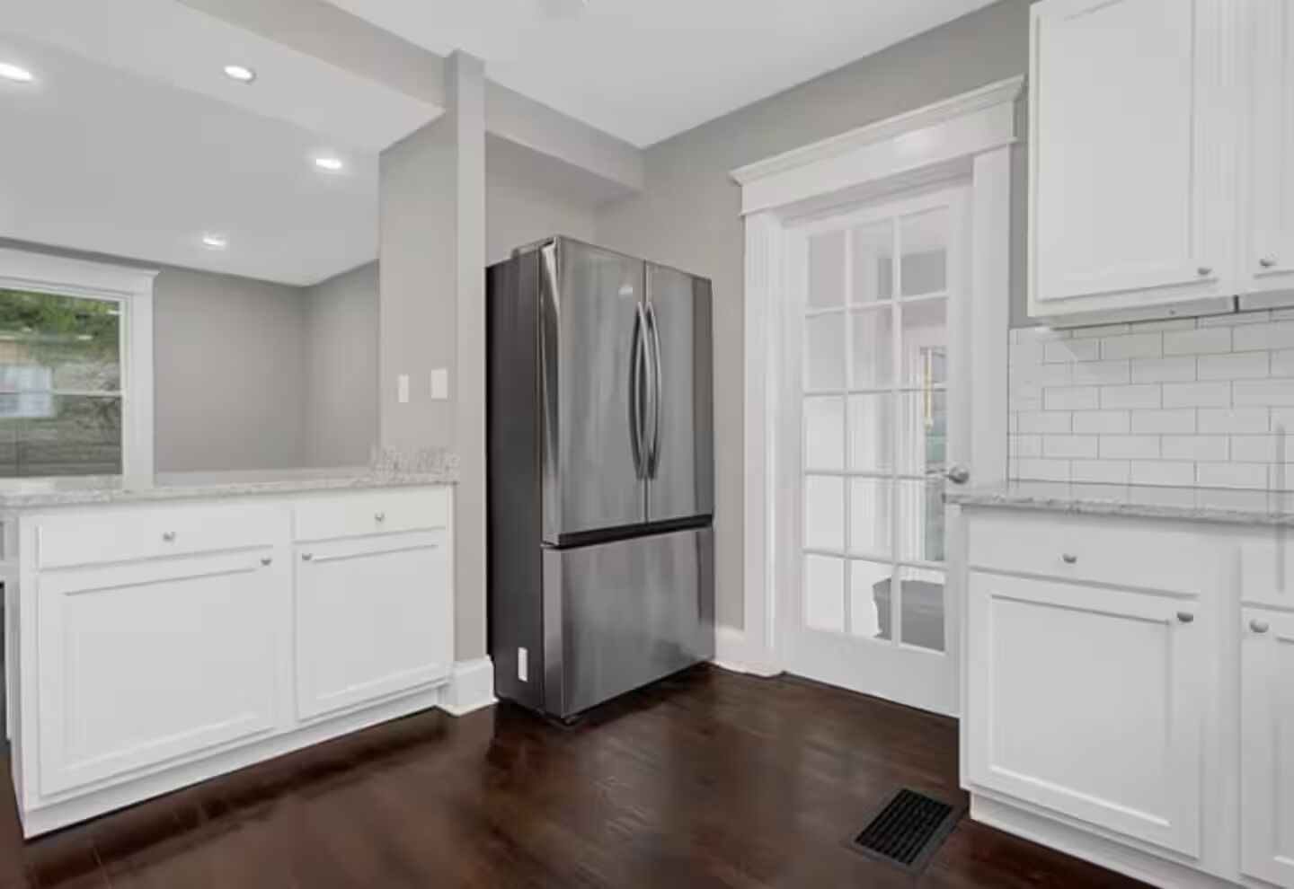 A kitchen with white cabinets, a stainless steel refrigerator, and a window with a view.