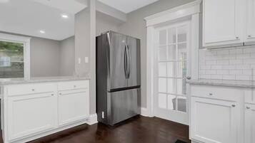 A kitchen with white cabinets, a stainless steel refrigerator, and a window with a view.