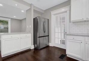 A kitchen with white cabinets, a stainless steel refrigerator, and a window with a view.