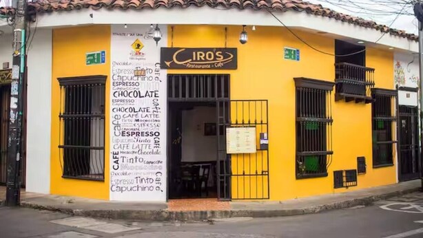 En gul bygning med et skilt der siger 'CIRO'S Restaurante - Cafe' og en menutavle, der viser varer som espresso, chokolade og cappuccino.