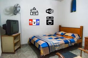 A bedroom with a bed, a TV on a stand, a fan, and wall icons indicating amenities like WiFi, laundry, and a TV. - Room with a private bathroom and kitchen (Cali)