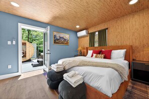 Ein Schlafzimmer mit Holzboden, einem Bett mit weißer Bettwäsche, einem Bild an der Wand und Blick durch eine offene Tür.