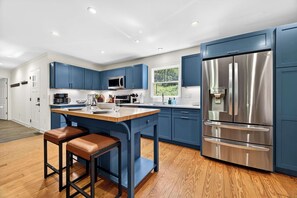 Eine moderne Küche mit blauen Schränken, Edelstahlgeräten, Holzboden und einem Barhocker.