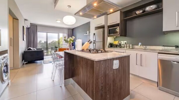 A modern kitchen with a central island, built-in appliances, and a dining area with a view. - The Hub Serviced Apts, Bryston Backup Power Wifi (Johannesburg)