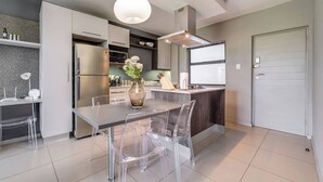 A modern kitchen with a dining area, featuring a central island, clear chairs, and a vase with flowers. - The Hub Serviced Apts, Bryston Backup Power Wifi (Johannesburg)