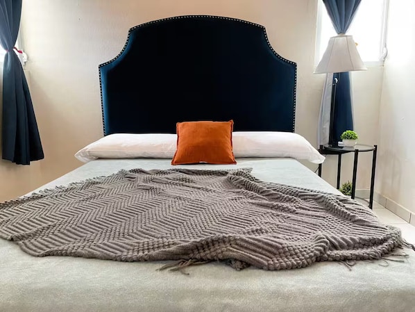 A bed with a dark headboard, a single orange pillow, and a textured blanket.