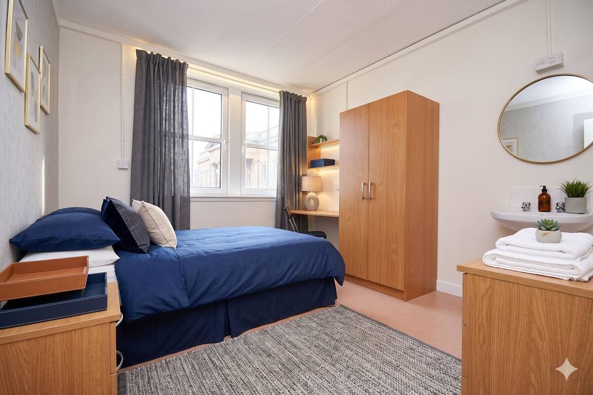 A bedroom with a bed, wooden wardrobe, bedside table, and a window with curtains.