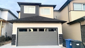 A two-story residential building with a garage, a driveway, and two trash bins. - Royal Oak- 2-bedroom Suite (Winnipeg)