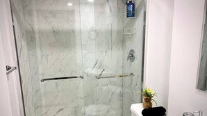 A modern bathroom with a glass-enclosed shower, a white toilet, and a sink with a mirror. - Royal Oak- 2-bedroom Suite (Winnipeg)
